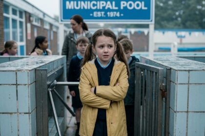 Jeune fille hésitante devant l'entrée d'une piscine municipale lors d'une sortie scolaire, bras croisés et expression anxieuse